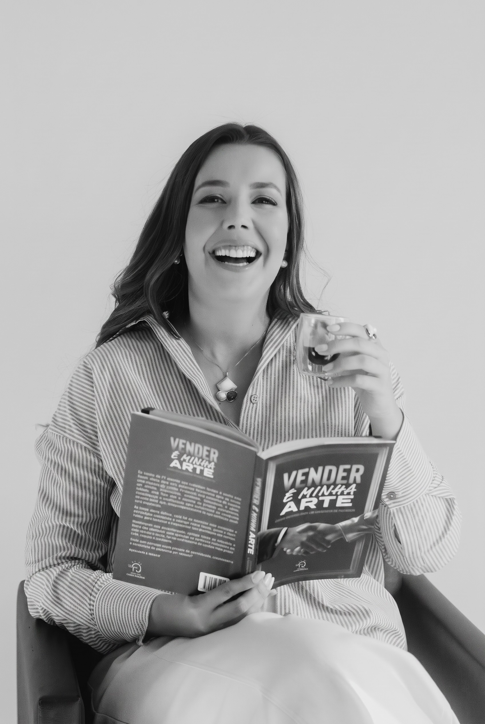 Raquel Perroni rindo com o livro Vender é minha Arte, em preto e branco